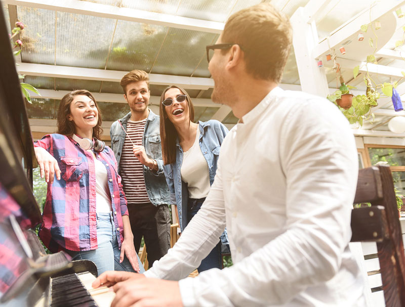 A man playing piano while friends listen and sing along